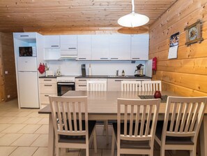 A modern kitchen with white cabinets, a built-in oven, and a dining area with a table and chairs. - Rukannaava 1a (2) by Interhome (Kuusamo)