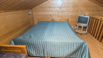 A small, cozy room with a bed, a television, and a wooden ceiling.