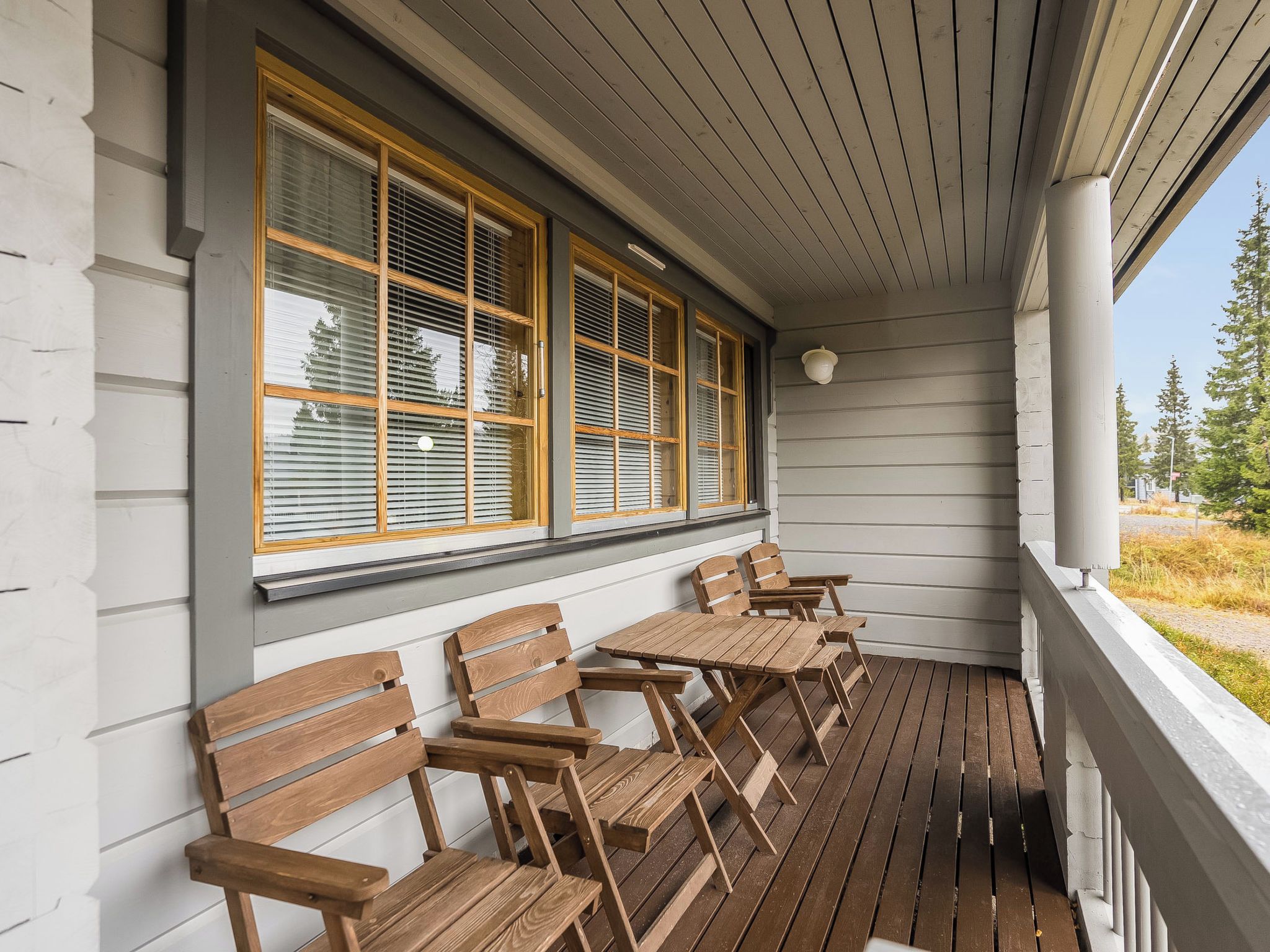 A wooden deck with benches and a table, overlooking a grassy area with trees.