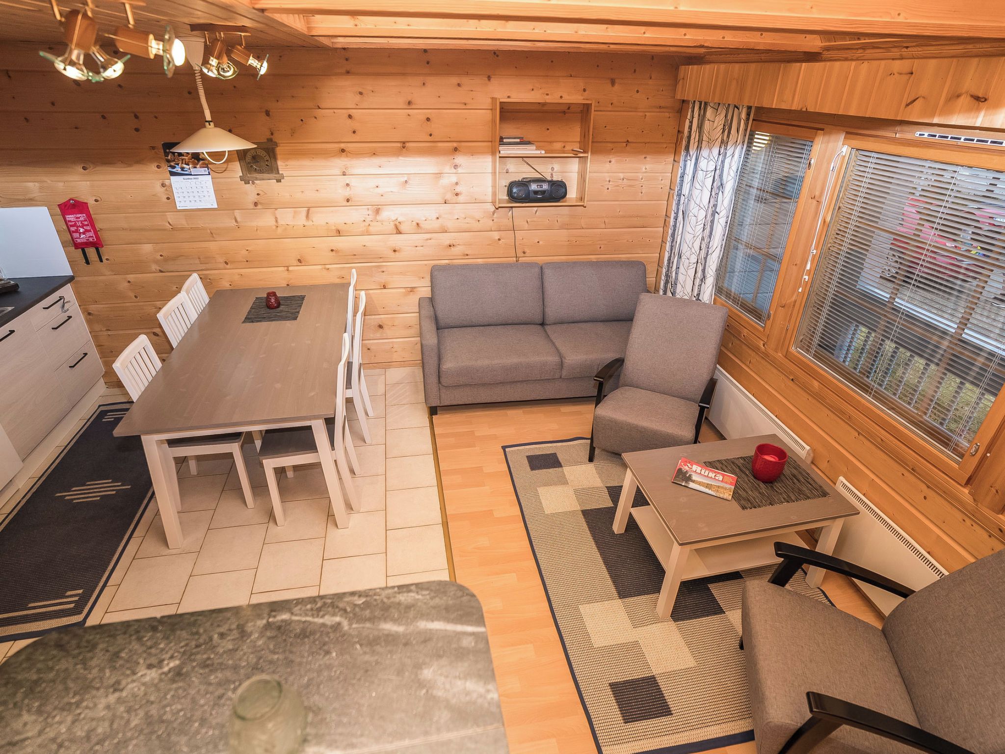 A cozy cabin interior with a dining area, sofa, and a window with blinds.