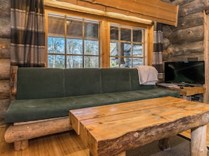 Interior de cabana de madeira com sofá verde, mesa de madeira e televisão.