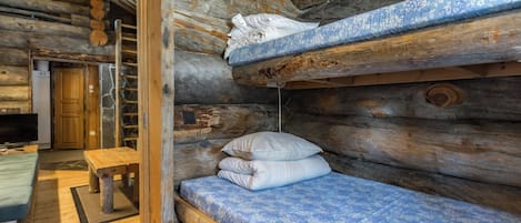 A log cabin interior with a bunk bed, a wooden bench, and a stone fireplace.