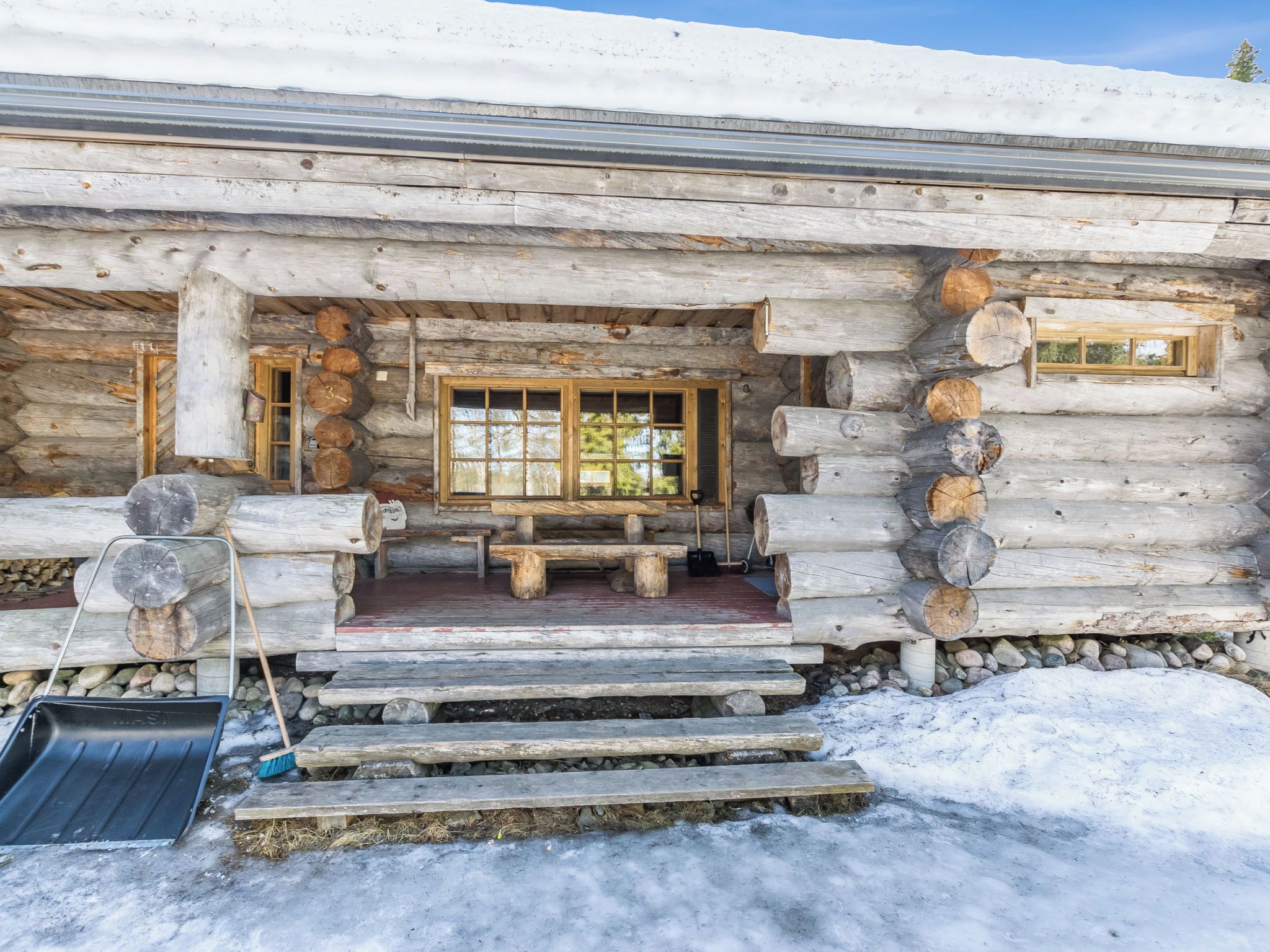A log cabin with a wooden porch, a bench, and a window.