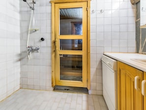 Casa de banho com porta de madeira, chuveiro e chão com mosaico branco.