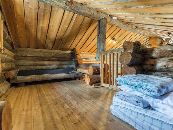 A log cabin interior with a wooden floor, a bed with blue bedding, and a fireplace with logs.