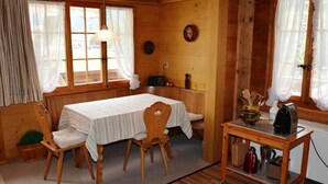 A cozy cabin-style room with a wooden interior, a dining table with chairs, a small kitchen area with a coffee maker, and a window with curtains. - Marmotte, Chalet by Interhome (Lauenen b. Gstaad)
