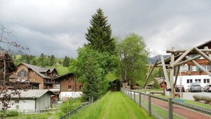 A rural village with traditional wooden houses, a tall tree-lined path, and a playground structure. - Marmotte, Chalet by Interhome (Lauenen b. Gstaad)