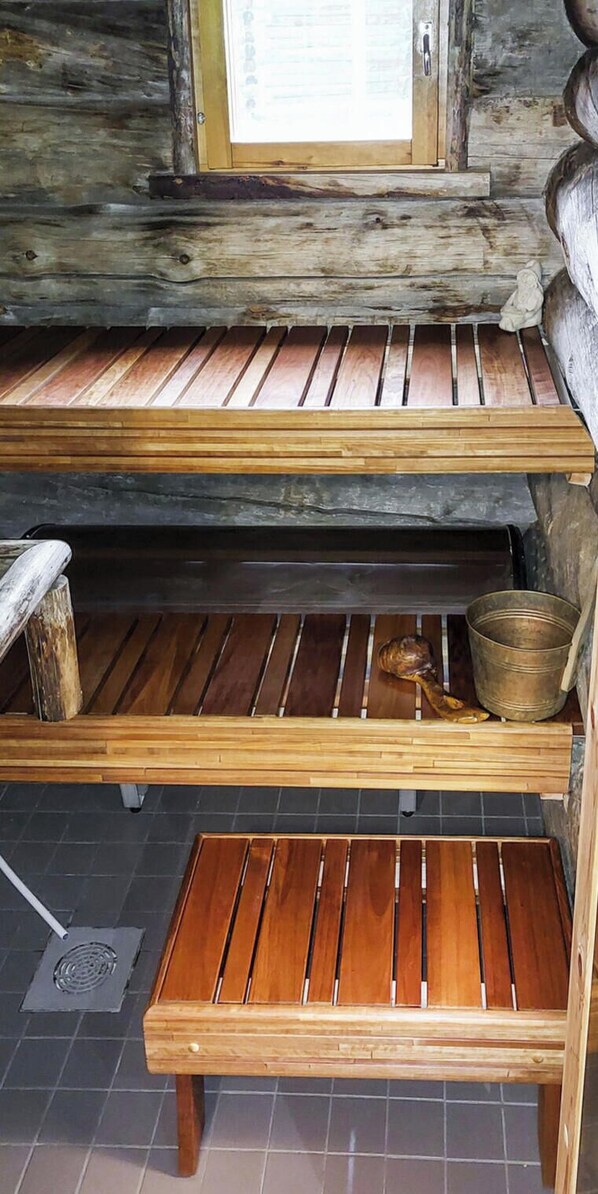 Un banc en bois pour sauna, accompagné d’un seau en métal et d’une bûche de bois.
