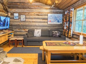 A log cabin interior with a wooden dining table, a sofa, a television, and framed pictures on the walls.