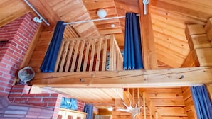 A wooden interior with a loft bed, a brick wall, and a ceiling with exposed beams.