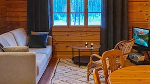 A cozy cabin interior with a sofa, two chairs, a small table, and a TV.