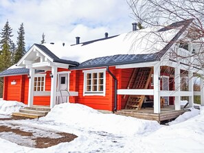 En röd och vit stuga med en inglasad veranda och ett trädäck.