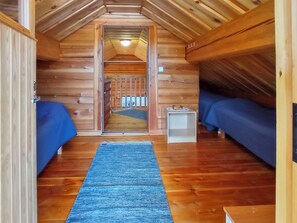 Interior de una cabaña con dos camas de madera, un tapete azul y una pequeña mesa.