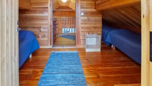 A cozy attic bedroom with wooden walls, a blue carpet, and two beds.