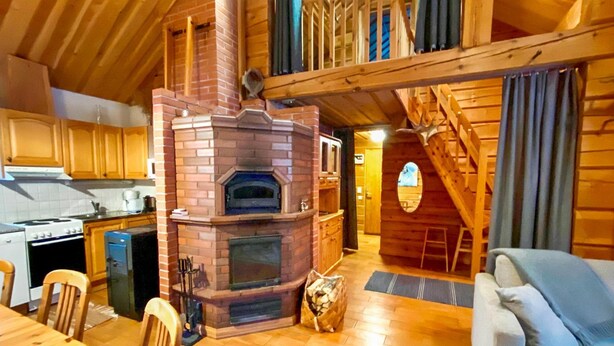 A cozy cabin interior with a fireplace, wooden furniture, and a staircase leading to an upper level.