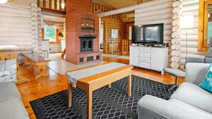 L’intérieur d’une cabane en rondins, avec une cheminée, un téléviseur et un coin repas.
