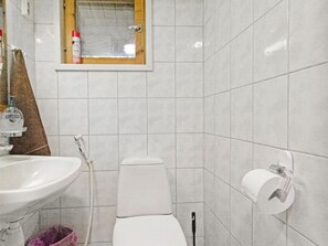 Une salle de bain avec un lavabo blanc, des toilettes et une petite fenêtre située au-dessus du miroir.