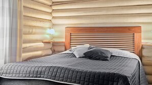 Une chambre dans un chalet en rondins, avec une tête de lit en bois, une lampe de chevet et un lit recouvert d’une courtepointe matelassée.