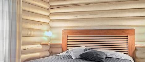 Un dormitorio de cabaña de madera con cabecera de madera, lámpara de noche y cama con cubrecama acolchado.