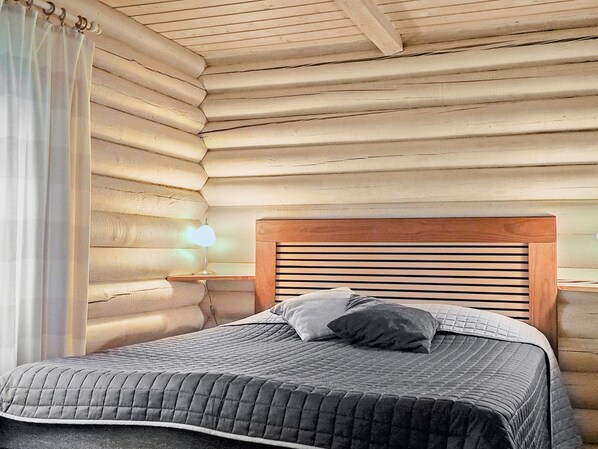 Ein Schlafzimmer in einer Blockhütte mit einem hölzernen Kopfteil, einer Nachttischlampe und einem Bett mit einer gesteppten Bettdecke.