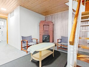 Ein Zimmer mit Holzboden, einem Kamin aus Backstein, zwei Holzstühlen, einer Bank und einer Treppe.