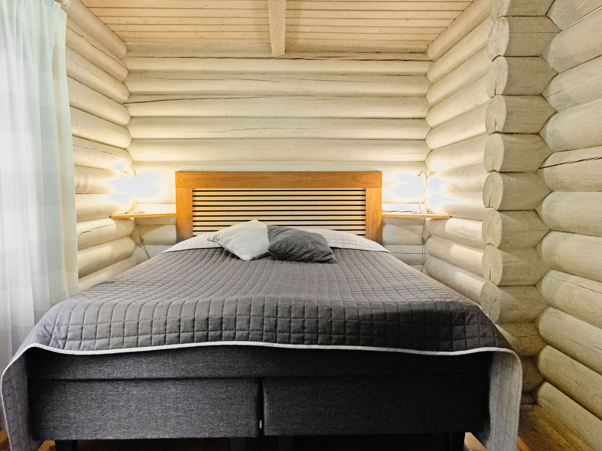 Una cama con cabecera de madera, dos lámparas de noche y una colcha acolchada.