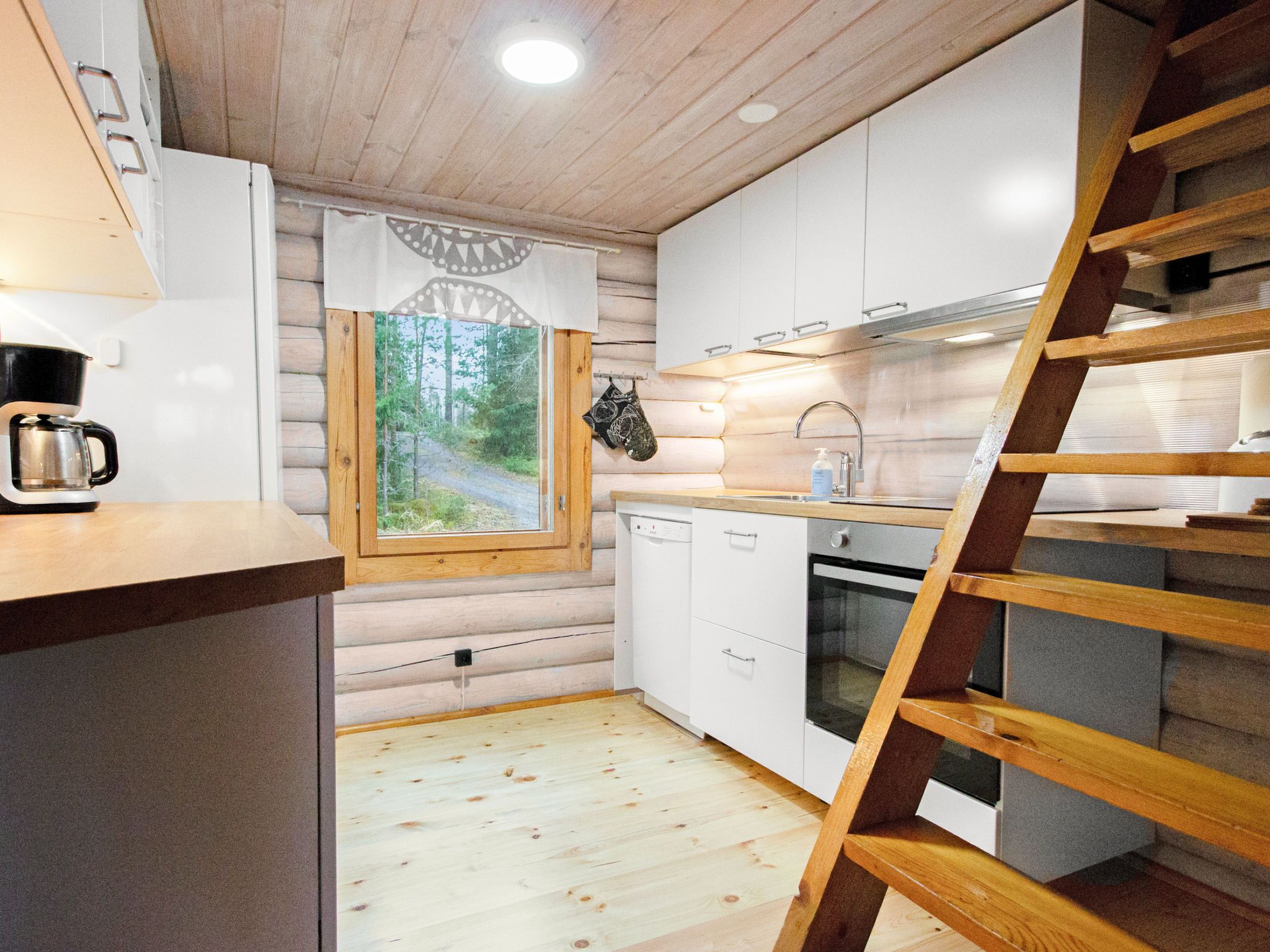 Eine kompakte Küche mit Holdekor-Schränken, einem eingebauten Backofen und einem Fenster mit Blick auf einen Waldweg.