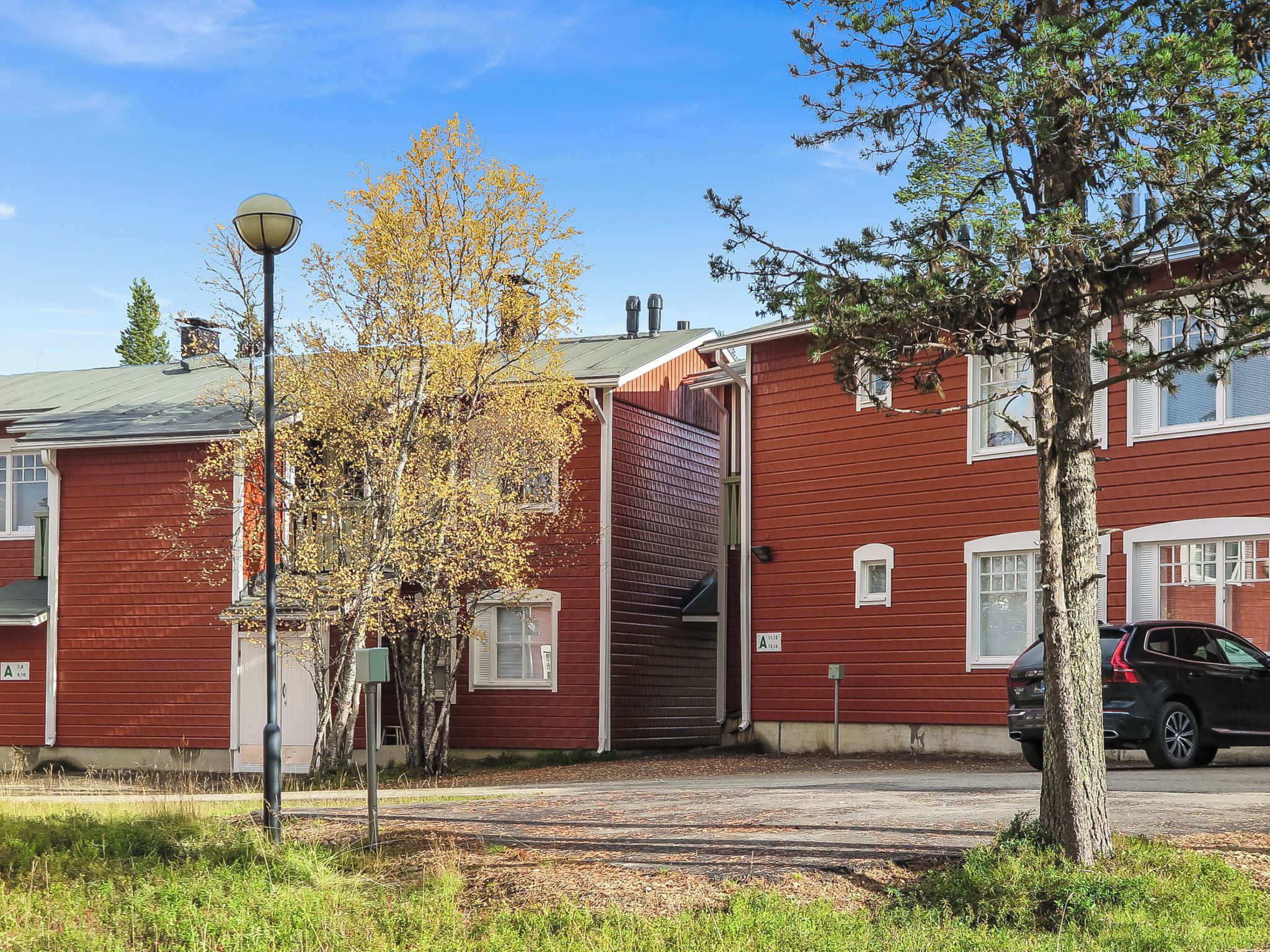A red building with a garage door, a street lamp, and a tree with yellow leaves.