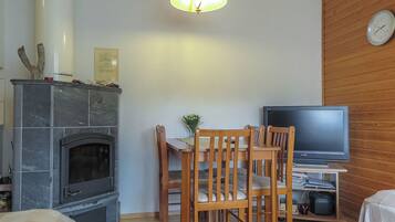 Een woonkamer met een open haard, houten stoelen, een televisie en een klok aan de muur.