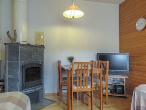 A living room with a fireplace, wooden chairs, a television, and a clock on the wall.