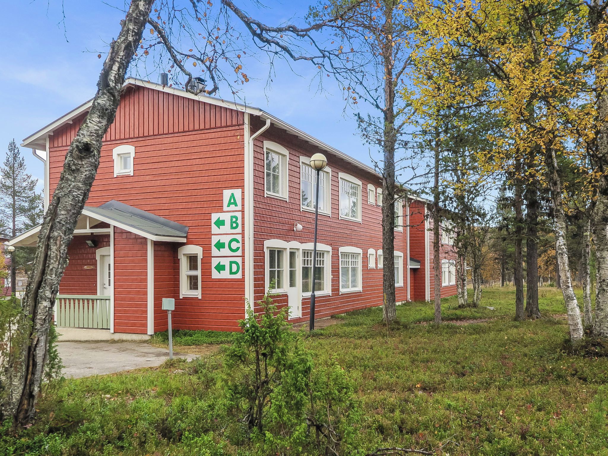 Een rode houten woning met veranda, omgeven door bomen en gras.