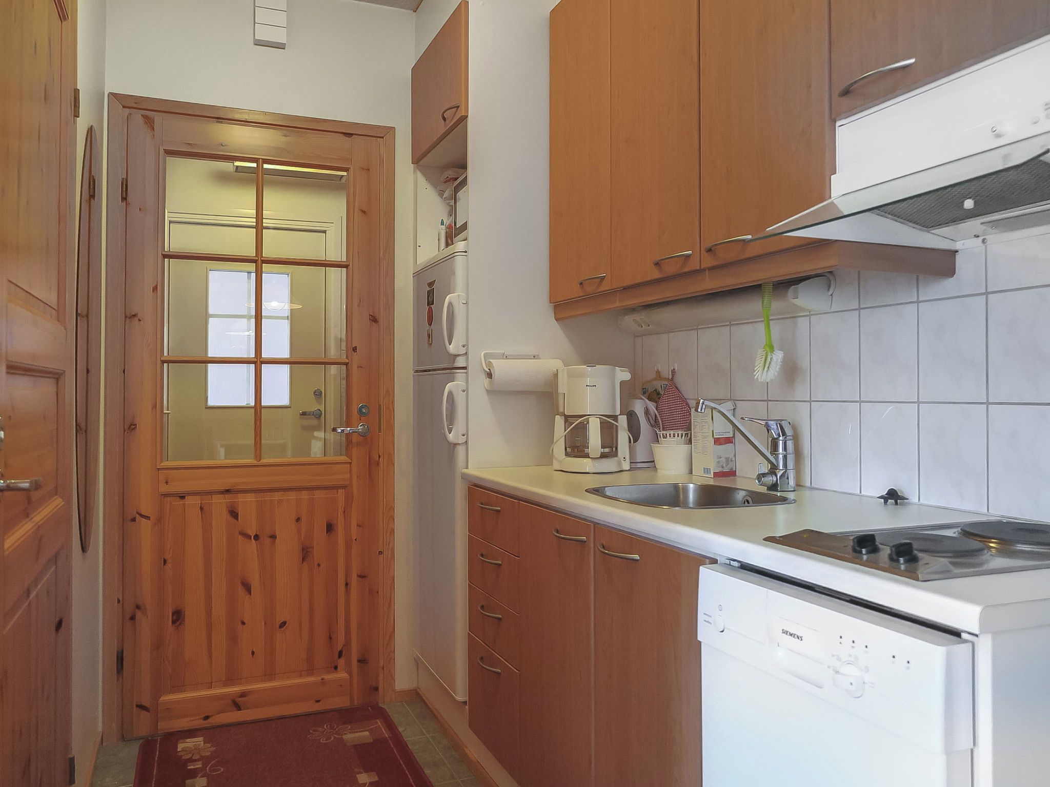 A compact kitchen with wooden cabinets, a built-in oven, a sink, and a coffee maker.