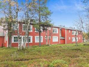 A red multi-story residential building with white window frames and a grassy front yard.