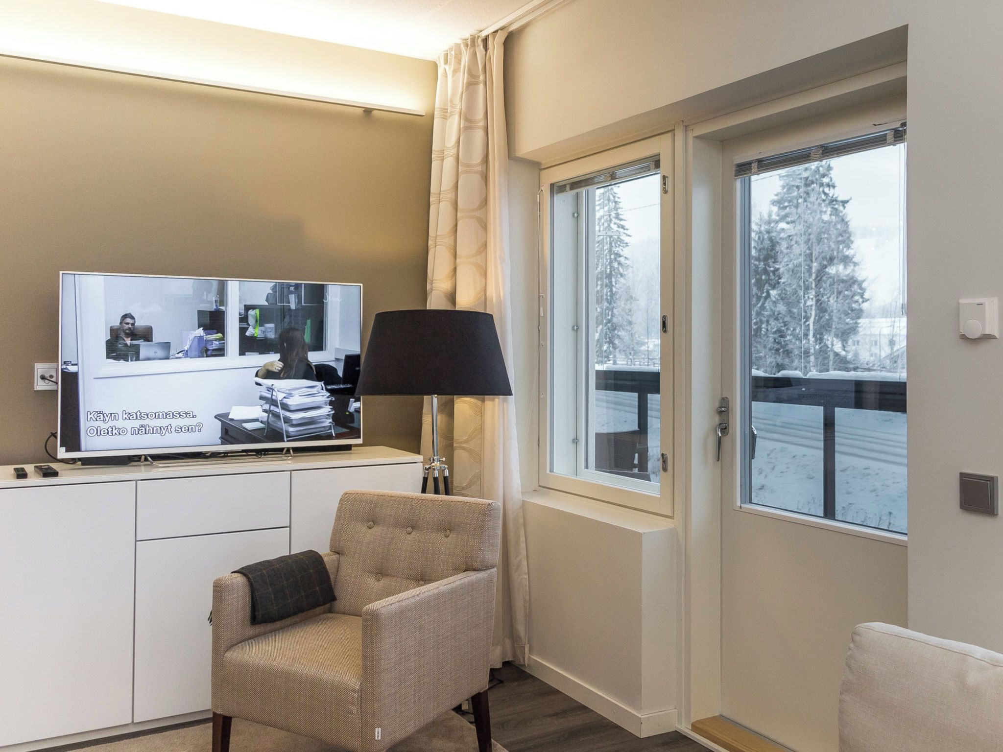 Een hotelkamer met een televisie, een lamp, een stoel en een raam met uitzicht op bomen.