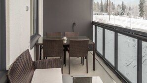 Un balcone con mobili in vimini, un tavolo in vetro e vista su un paesaggio innevato.