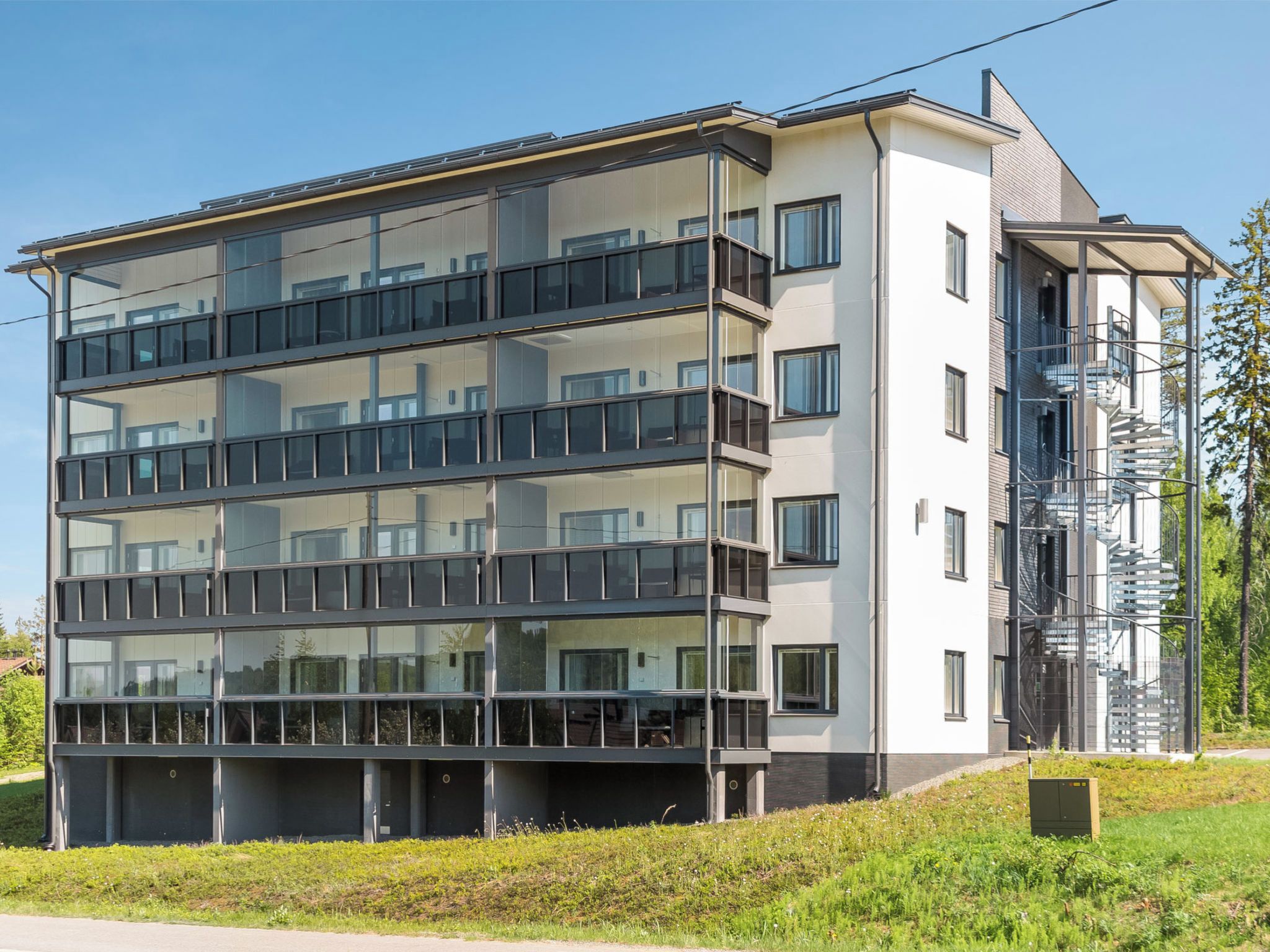 A multi-story residential building with balconies, a fire escape, and a green landscape.