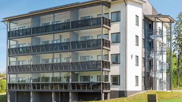 A multi-story residential building with balconies, a fire escape, and a green landscape.