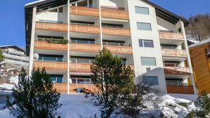 A multi-story hotel with balconies, a ski slope in the background, and snow on the ground.
