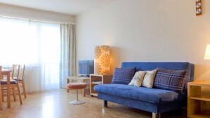 A modern living room with a blue sofa, a wooden dining table, and a TV.