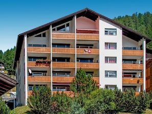 A multi-story hotel with balconies, a ski resort in the background, and a clear sky. - Beaulieu by Interhome (Zermatt)