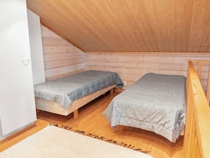 A small, single-room cabin with two wooden beds, a white wall, and a wooden ceiling.