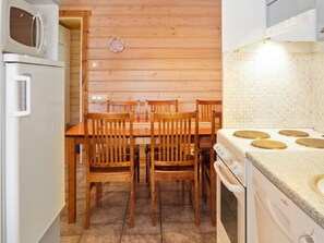 A wooden interior with a dining table and chairs, a microwave, a stove, and a clock on the wall.