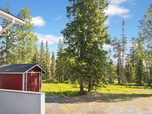 A red shed with a white door, surrounded by a grassy area with trees.