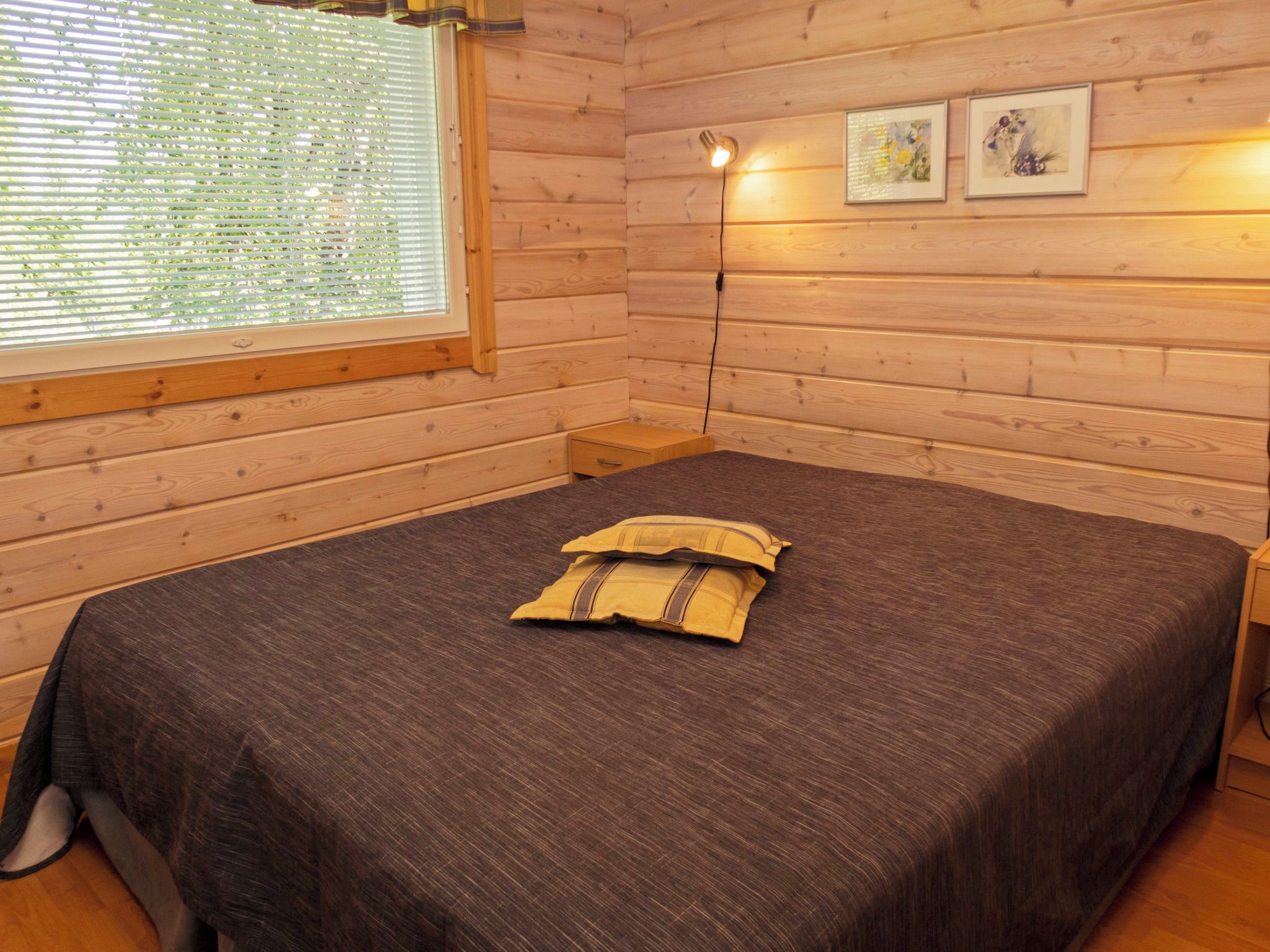 Una habitación con paneles de madera, una cama, una mesita de noche, una lámpara y dos cuadros en la pared.