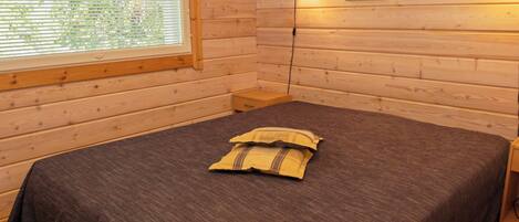 Una habitación con paneles de madera, una cama, una mesita de noche, una lámpara y dos cuadros en la pared.