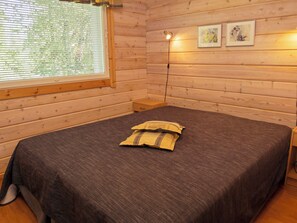 A wooden-paneled room with a bed, a nightstand, a lamp, and two framed pictures on the wall.