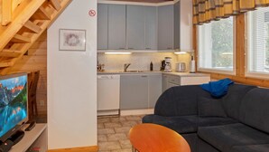 A compact living space with a kitchenette, a sofa, a TV, and a wooden table.