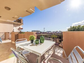 A rooftop terrace with a table and chairs, a potted plant, and a green kettle.