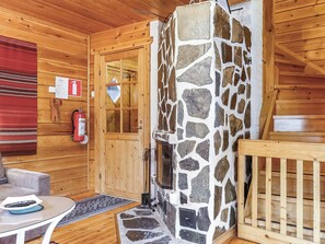 Interior de una cabaña de madera con chimenea de piedra, una puerta de madera, un extintor y una manta roja en la pared.