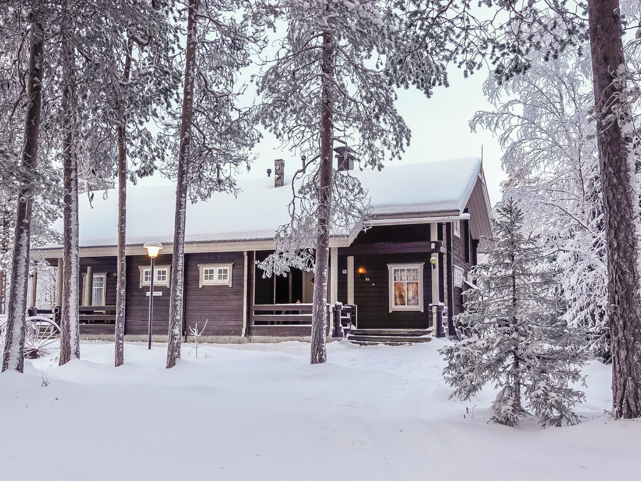 A wooden cabin with a porch, surrounded by snow-covered trees.